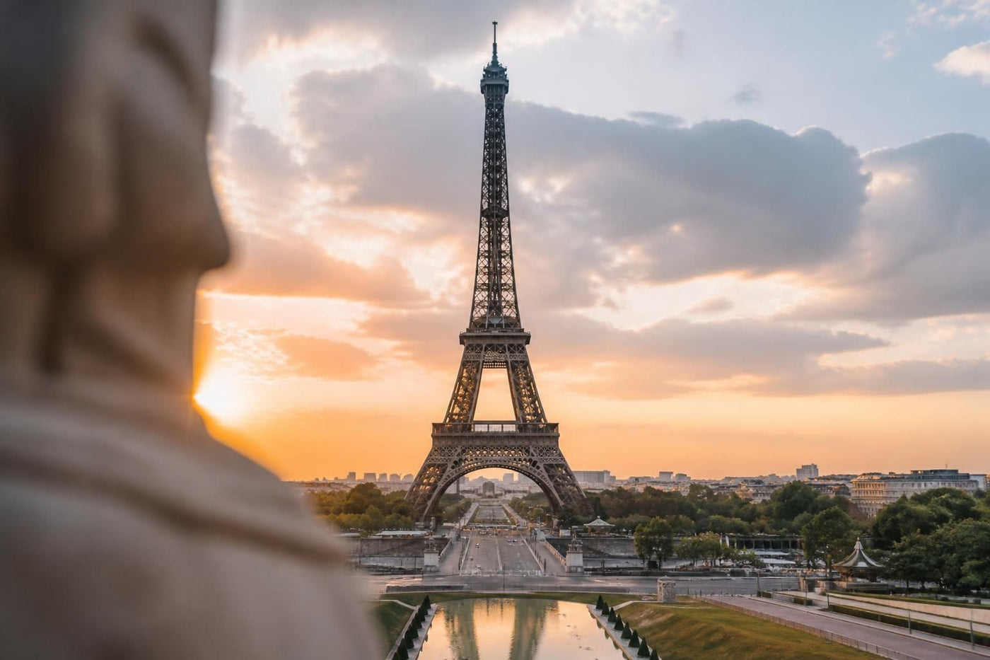 The Eiffel Tower at golden hour above the Champ de Mars in Paris, with the Seine and Haussmannian rooftops in the background