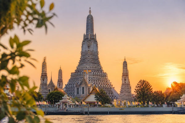 Golden spires of Wat Arun temple beside the Chao Phraya River in Bangkok, Thailand, at sunset